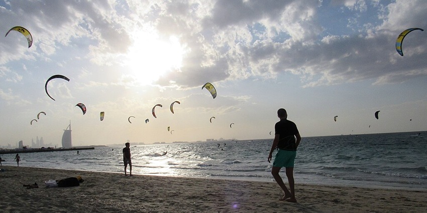 Kitesurfers on a beach at sunset, with kites in sky and the Burj Al Arab in the distance