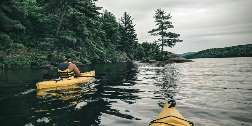 Two people with safety jackets sitting in a kayak and both holding the paddles at the deepest lake in Michigan, Torch Lake.