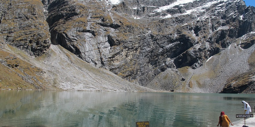 Hemkund lake with clear waters, a small sign board and two women standing near the shore