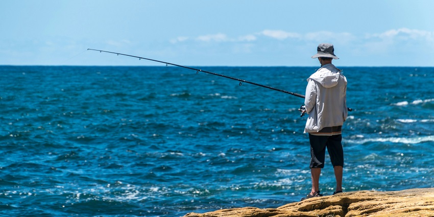 Person holding the hook of a fishing rod and the rod lying on a rocky