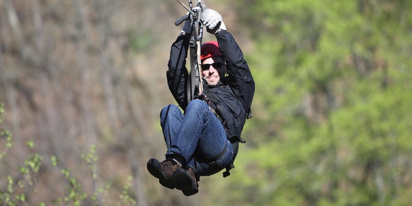 Image of a man enjoying zipline ride in an adventure park surrounded by lush greenery