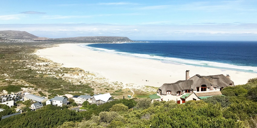 A wide view of Noordhoek Beach with mountains in the background and a peaceful shoreline.