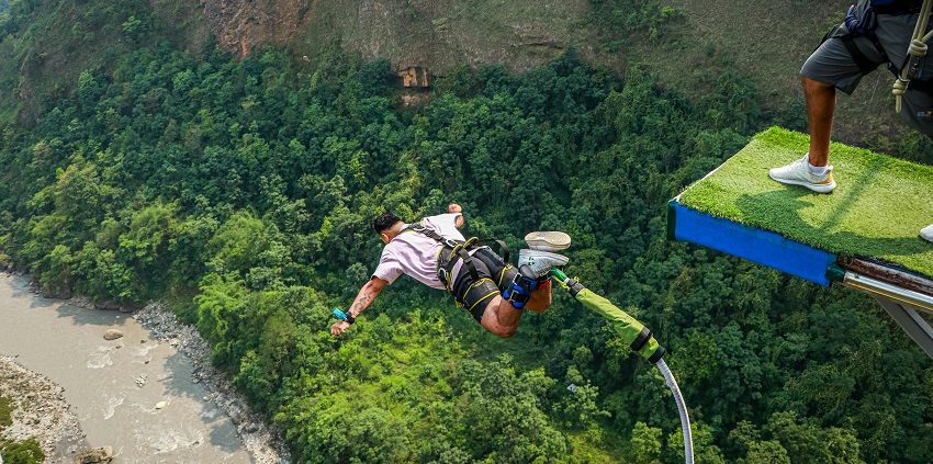 A man suspended on a rope, during bunjee jumping in South Goa, with a scenic landscape in the background.