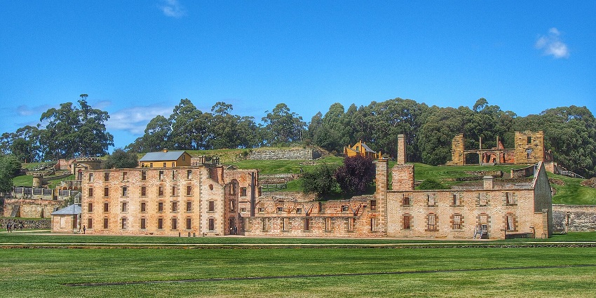 Hobart Convict Penitentiary, an old brick building amidst greenery and a clear blue sky background.