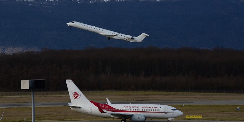 Commercial jet planes take off from the airport with scenic mountain views and a busy runway.