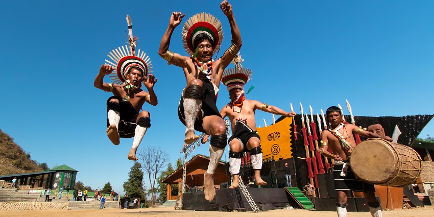 An image of individuals in traditional attire performing a cultural dance, captured in a dynamic jump, during the Hornbill Festival of Nagaland.