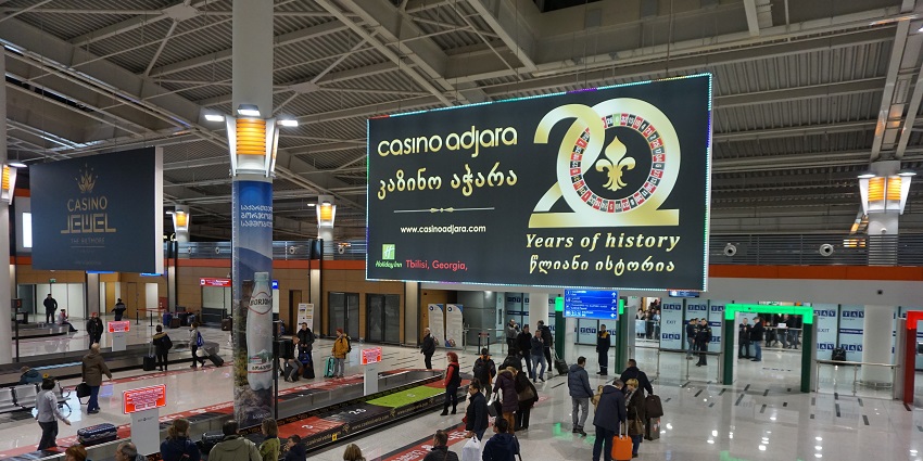 Image of Tbilisi International Airport baggage claim area with passengers standing and waiting