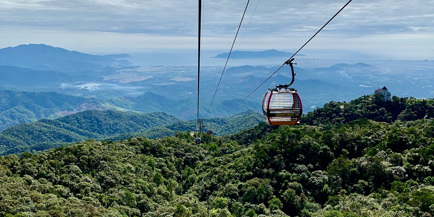 An aerial view of a cable car with lush green meadows in the background in the day.
