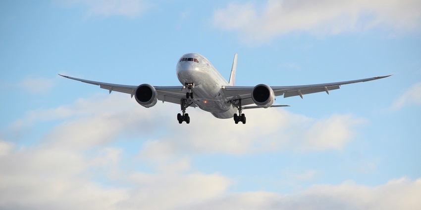 Image of a grey aeroplane flying in the clear sky during the daytime surrounded by clouds.
