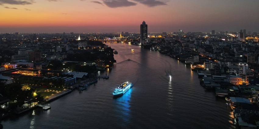 A photo of the Chao Phraya River Cruise floating along Bangkok's skyline all through the night.