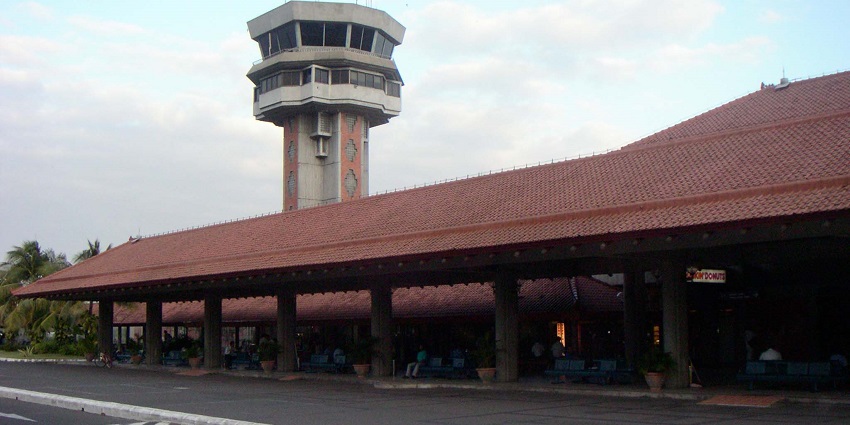 Airport terminal with red-tiled roof and a control tower against a partly cloudy sky.