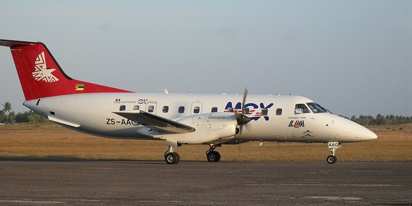 Small white propeller aircraft on the runway of Inhambane airport with sandy plains in the back