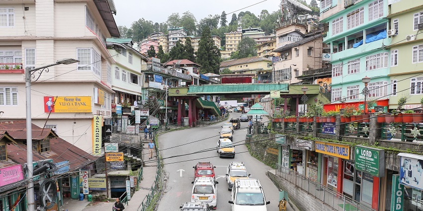 Several taxis pass through the road with buildings on both sides and a walking area.