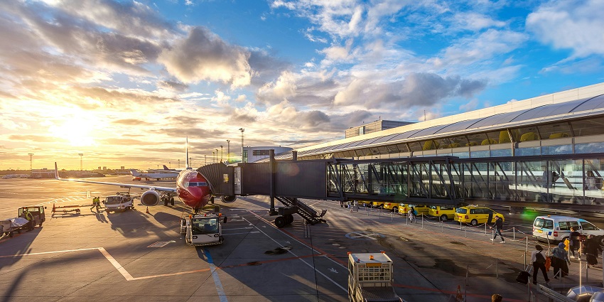 Airport with a red aeroplane connected to the passenger boarding bridge and cars parked