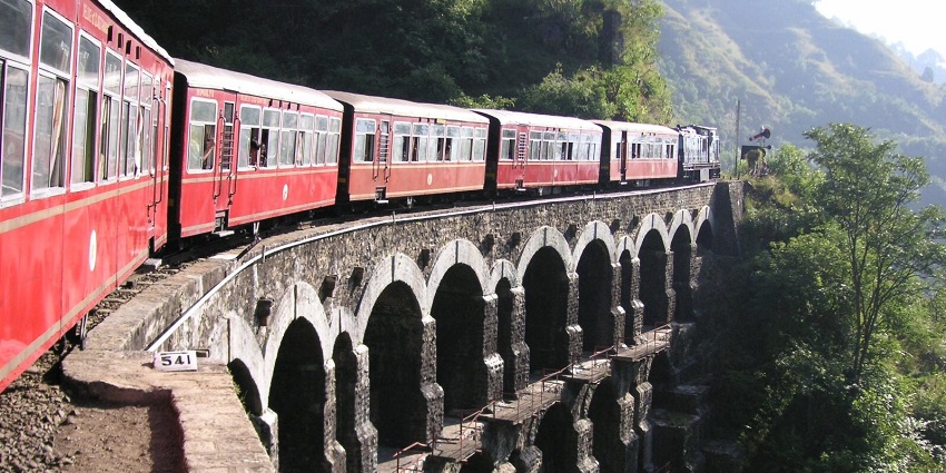 Red train passing through the heritage bridge between Kandaghat and Kanoh on a green hill