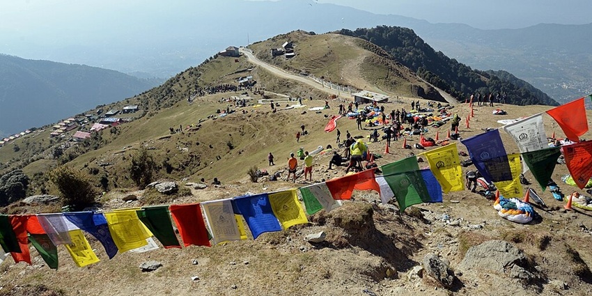 An image of colourful prayer flags and people on the hillside in Bir Billing, the highest paragliding in India, with a beautiful mountain view.