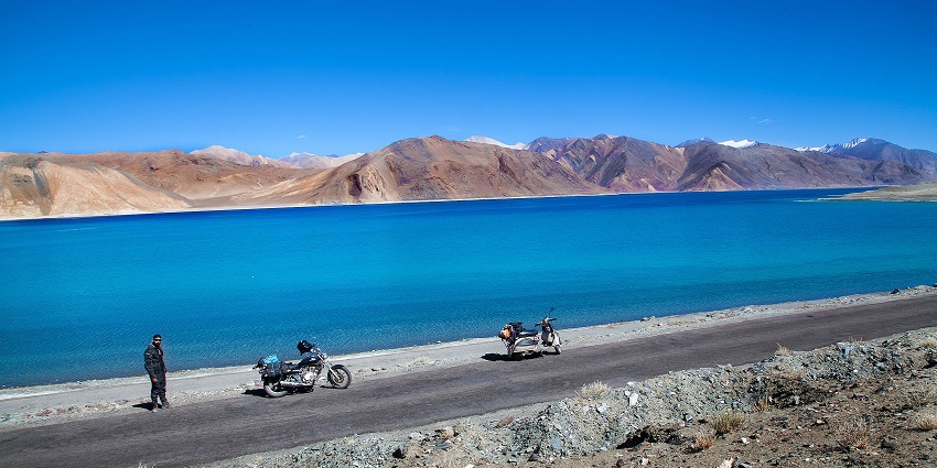 Road near the Pangong Tso Lake with two motorcycles parked on the road and a man standing