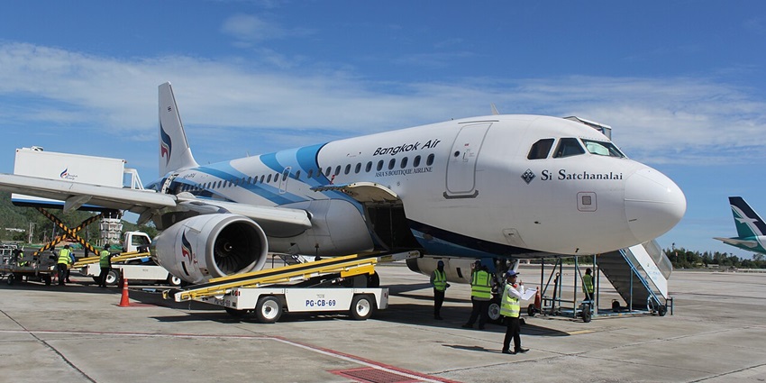 An aeroplane at Koh Samui Airport (USM), surrounded by lush greenery and blue skies.