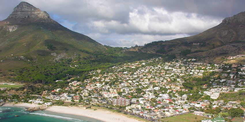 An image of a sunset over the rocky coastline of the Camps Bay Beach, with vivid orange, red hues, and crashing waves.