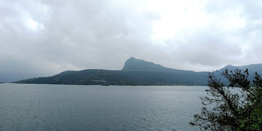 View of the scenic shore of Pawna lake, with misty mountains in the far background