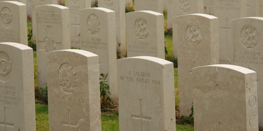 War cemetery with multiple tombstones, carvings on the tombstones and green grass.