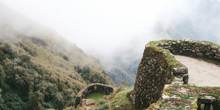 A girl standing on the Inca Trail overlooking Machu Picchu with mountains and clouds.