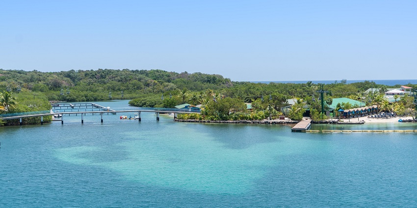 Cars are crossing a long bridge in Roatán, with blue waters and lush green scenery around