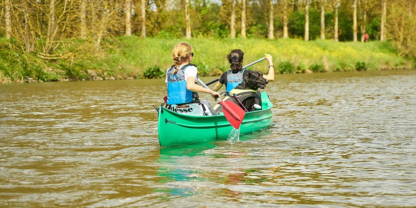 Two women in a kayak with a green kayak, holding the paddles and blue safety jackets