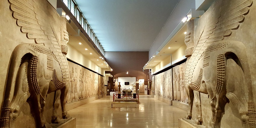 Museum hallway with large, winged bull statues on each side, and a display case