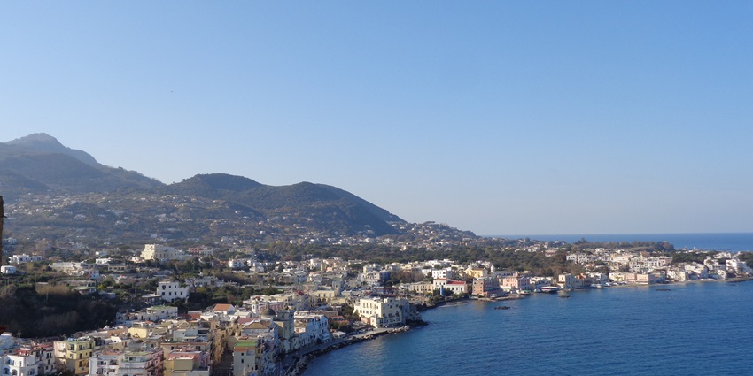 Scenic view of Ischia with lush hills, colourful buildings, and crystal-clear blue waters