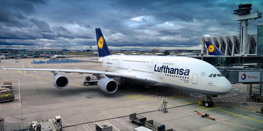A fleet of aeroplanes await their journey on the runway near the airport during the daytime.