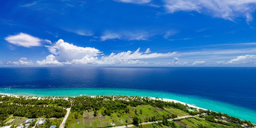 Island covered in greenery and surrounded by a sandy shoreline and a vast blue sea