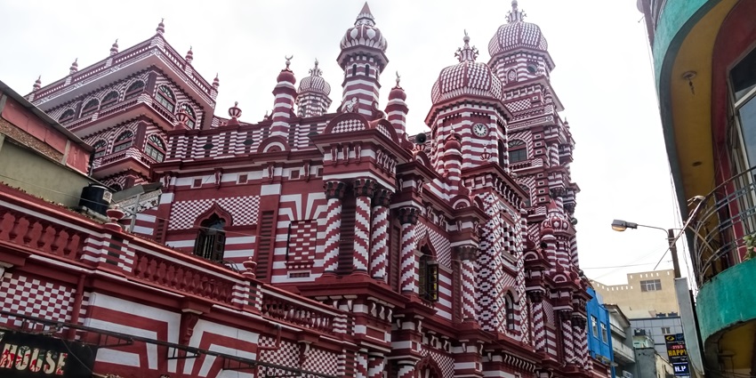 An image of the Jami Ul-Alfar Mosque with red and white striped walls, adorned with domes