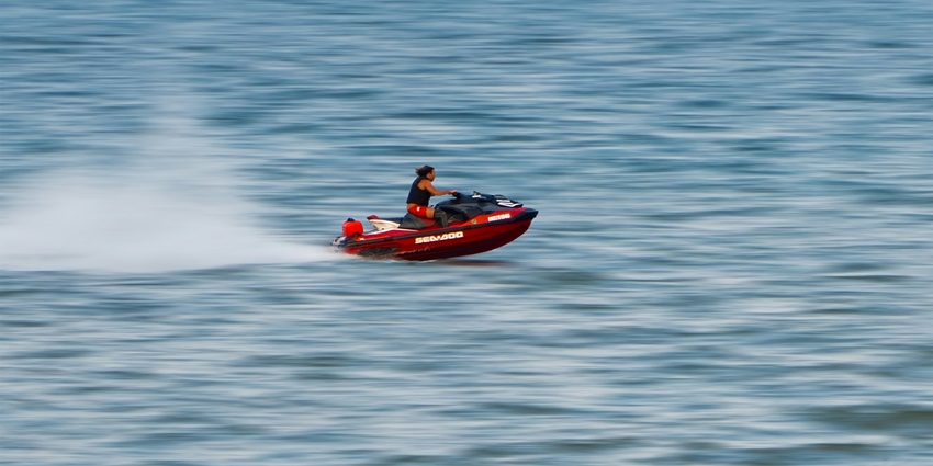 Image of a man riding a jet ski across a calm lake in Oakville, Canada, under a clear sky