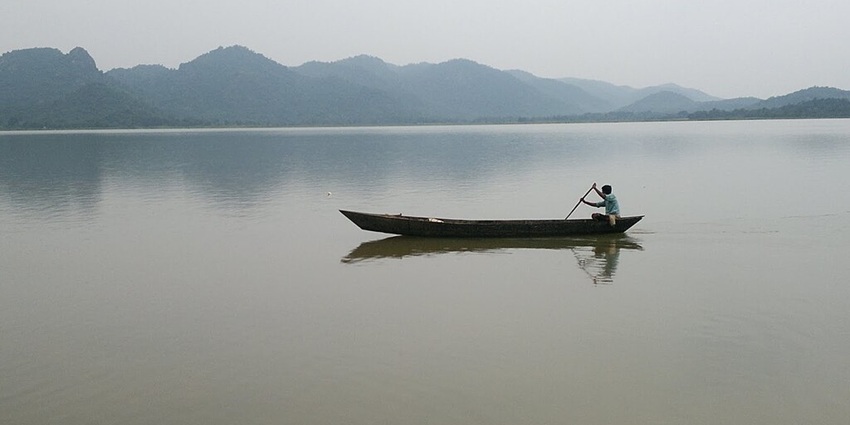 Lake with a still and large water body, a man rowing in the boat and offshore mountains