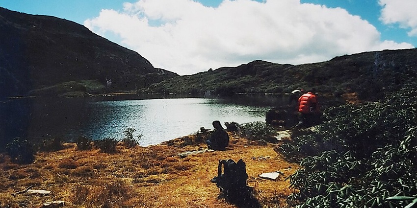 Man sitting on the shore of Jimilang Tsho, gazing at the lake, with two others nearby