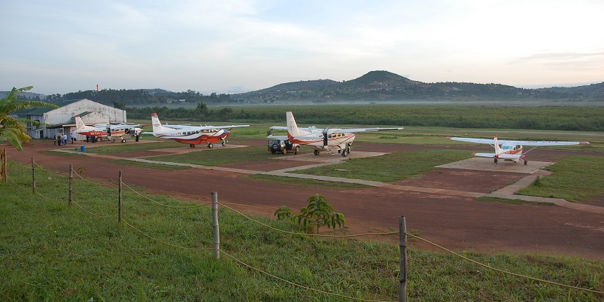 Multiple propeller aeroplanes parked on the sandy airstrip, airstrip building and distant hills