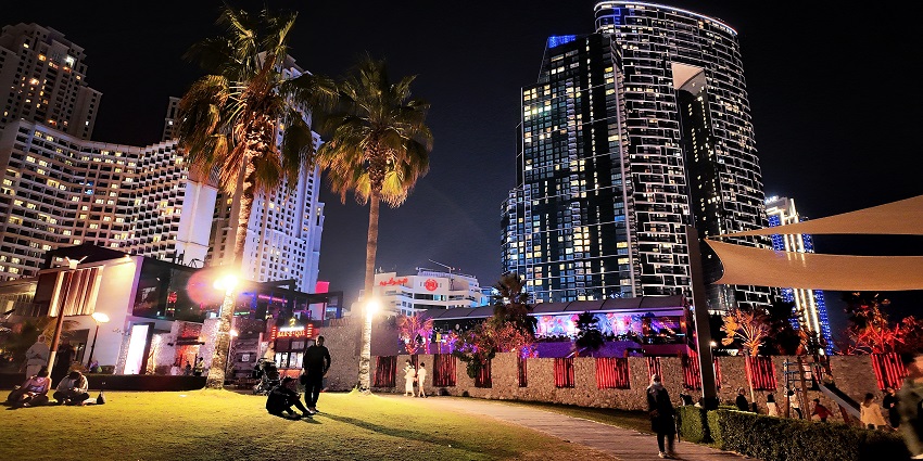 Night view of illuminated skyscrapers and palm trees in Dubai Marina with people relaxing