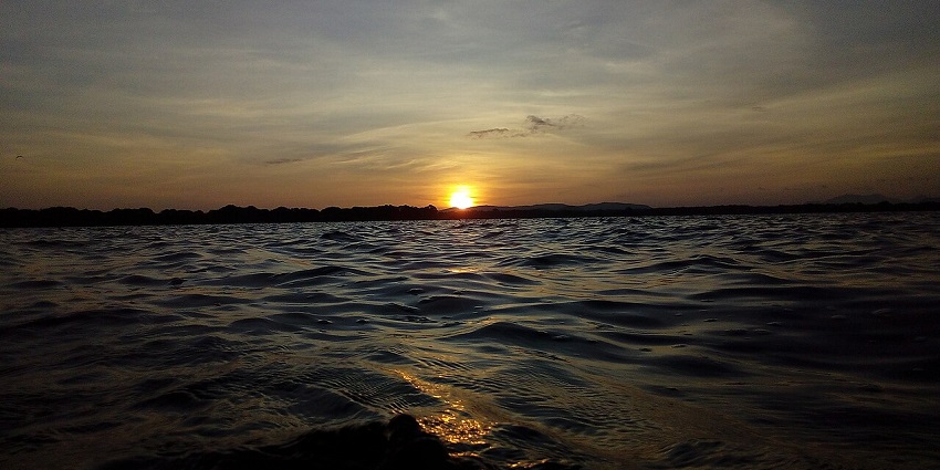 Sunset over the Kala Wewa reservoir, with gentle ripples on the water's surface.