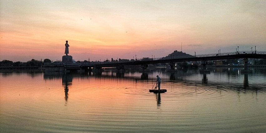 Lake with a large water body, a bridge over the lake, a person on the water and a statue