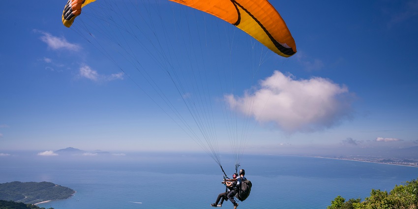 A person paragliding over a coastal landscape with a bright orange parachute in Kamshet.