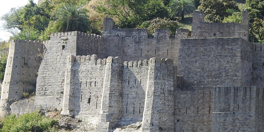 An image of an ancient stone fortification of the Kangra Fort, featuring defensive battlements and towers.