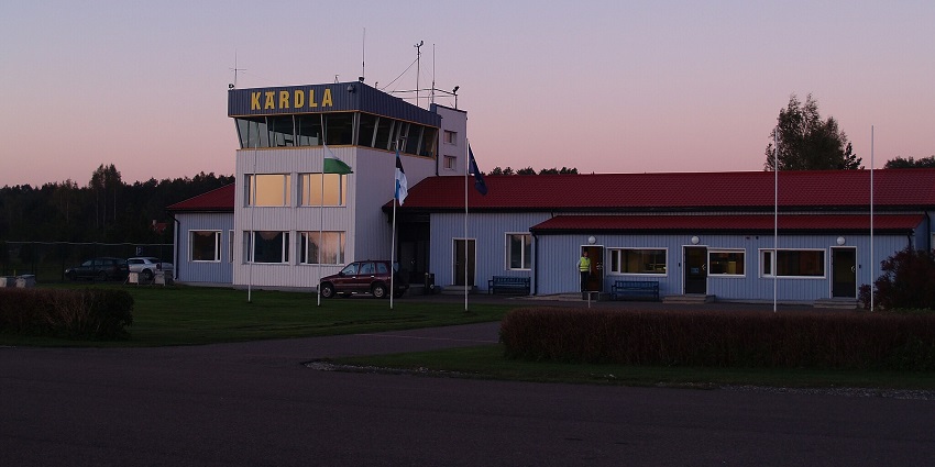 Kärdla Airport in red and white, with parked cars and a watchman securing the entrance