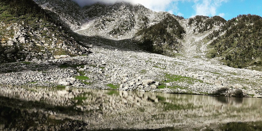 Kareri Lake with a perfect reflection of a rocky shoreline and mountains covered in clouds