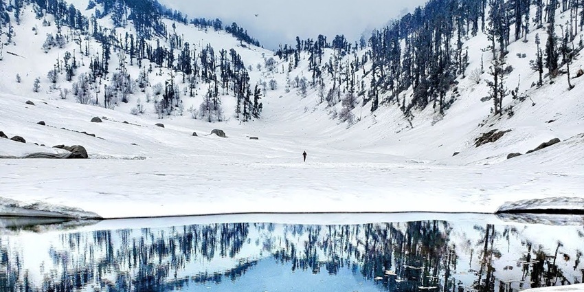 Frozen mountain lake surrounded by snow-covered peaks under a clear blue sky.