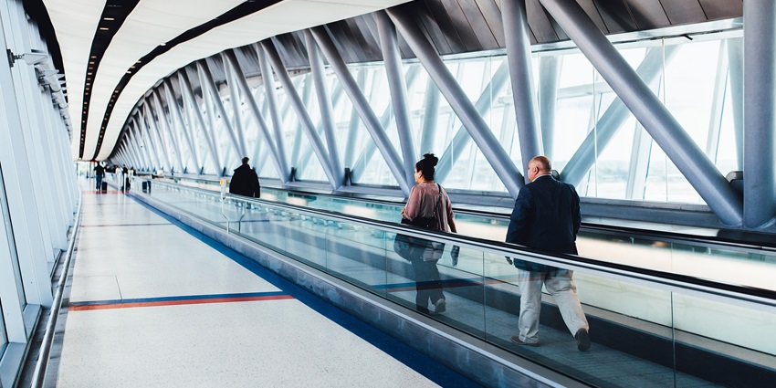 Passengers walking at distances inside a less crowded airport with bags on their shoulder