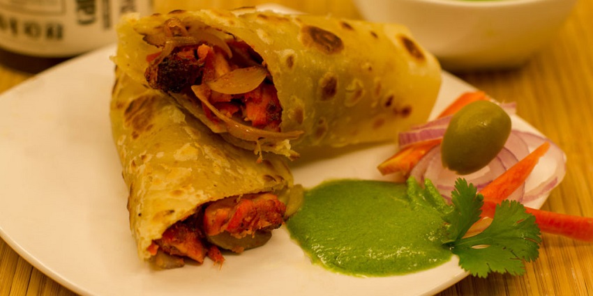 An image of a Kathi Roll, a wrap filled with strips of carrots and other ingredients, placed on a tray
