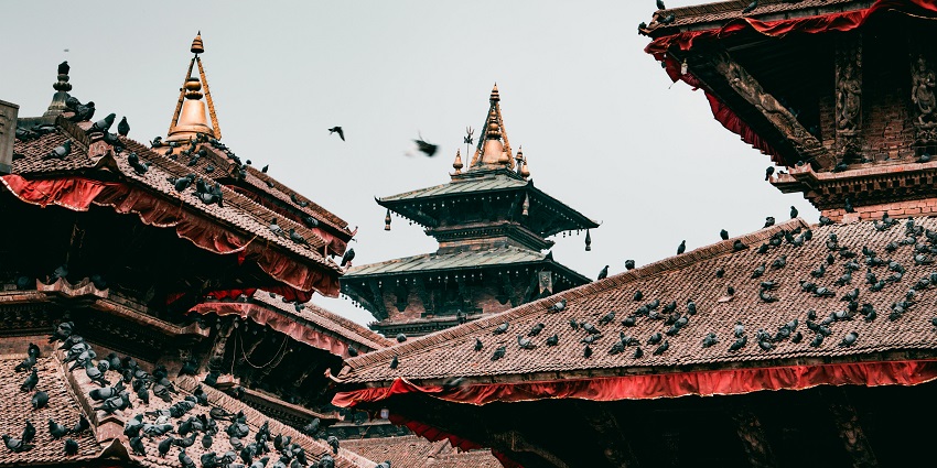 Temples of Kathmandu Durbar Square, adorned with red fabric and pigeons on rooftops.