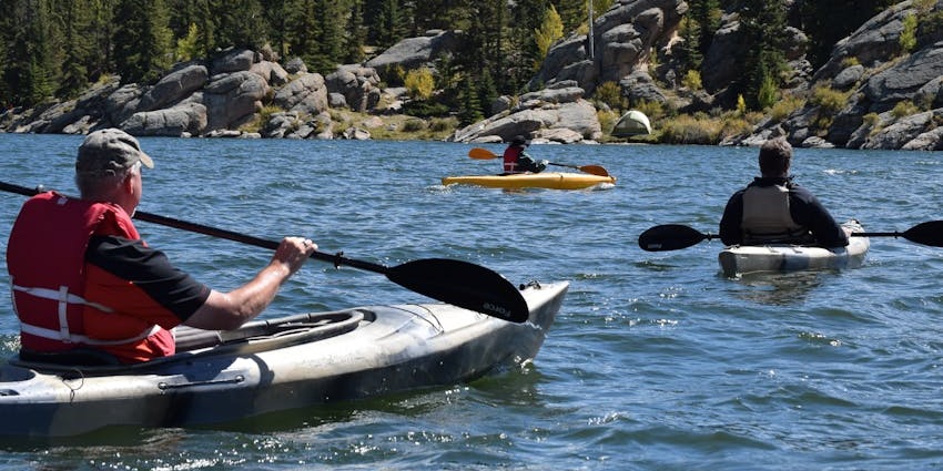 Multiple people kayaking in kayak boats holding the paddles with distant green shorelines