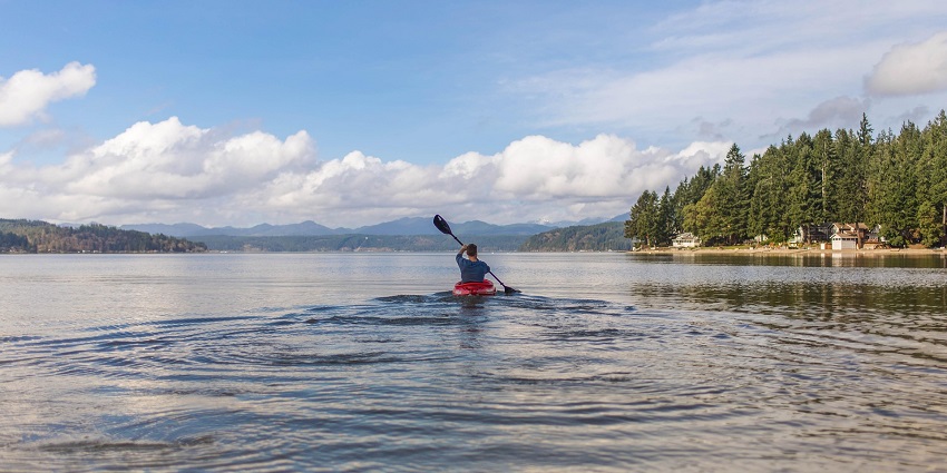 An image of a man in a blue t-shirt kayaking alone in the calm water during daylight